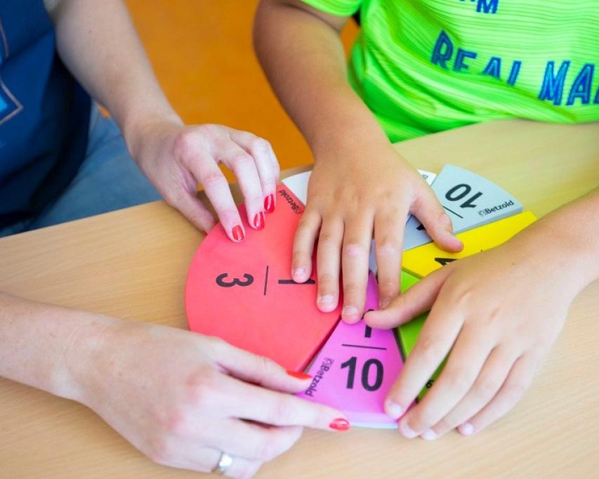 Leerkracht met leerling met voelbaar rekenmateriaal in de klas