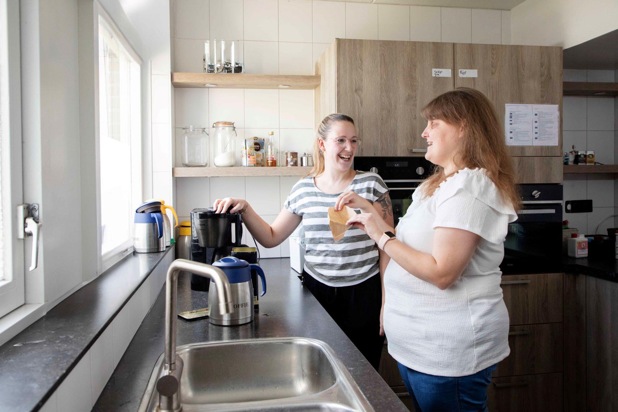 Twee jonge vrouwen praten bij bij een koffiezetapparaat