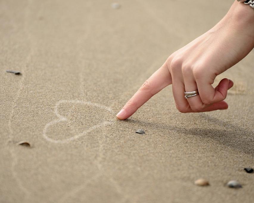 Iemand tekent met zijn vinger een hart in het zand