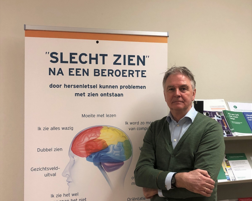 Optometrist Henk Stam bij een poster over problemen met zicht na een beroerte.