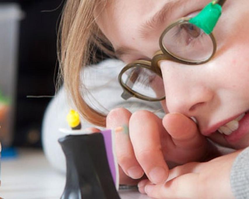 leerling met bril kijkt van dichtbij naar poppetje op bureau