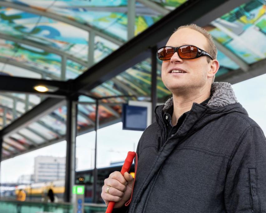 Man met blindegeleidestok en smartphone op NS station.