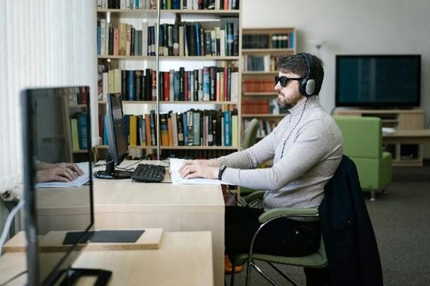 Een man werkt op zijn computer aan een bureau met behulp van een braille toetsenbord