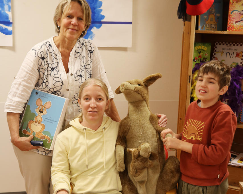 Auteur Hannelies, ervaringsdeskundige Melanie en leerling Jonas op de foto met een knuffel kangoeroe en het boek