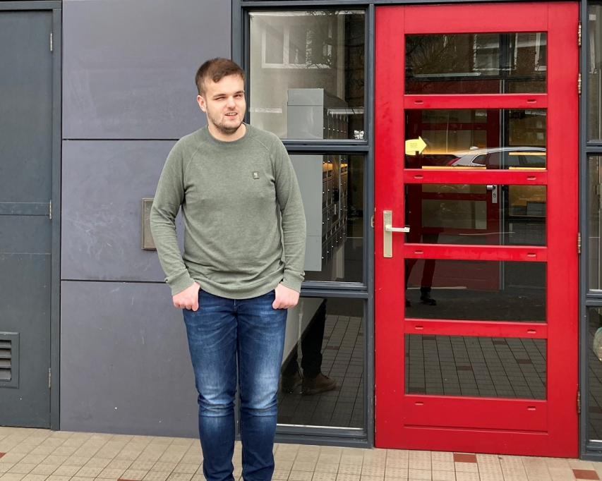 Stan poseert bij de felrode voordeur van het kamertrainingscentrum