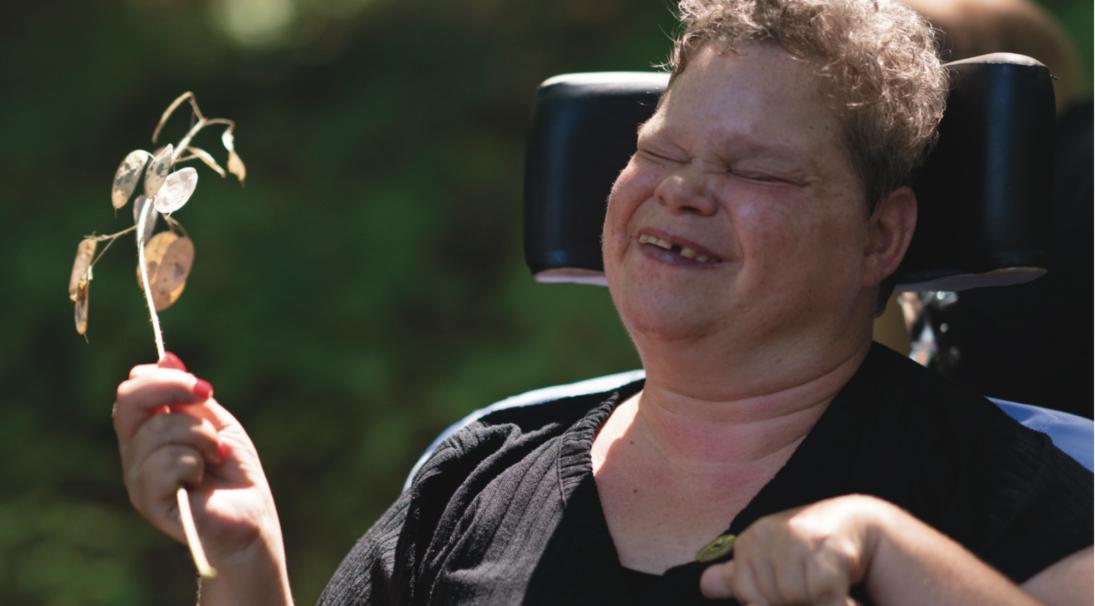 Een bewoner van Bartiméus met een takje met blaadjes in haar hand.