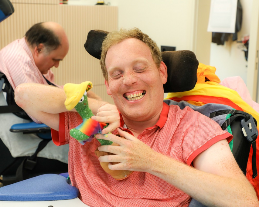 Man in rolstoel houdt speciale knuffel van het FabLab vast. Hij lacht.