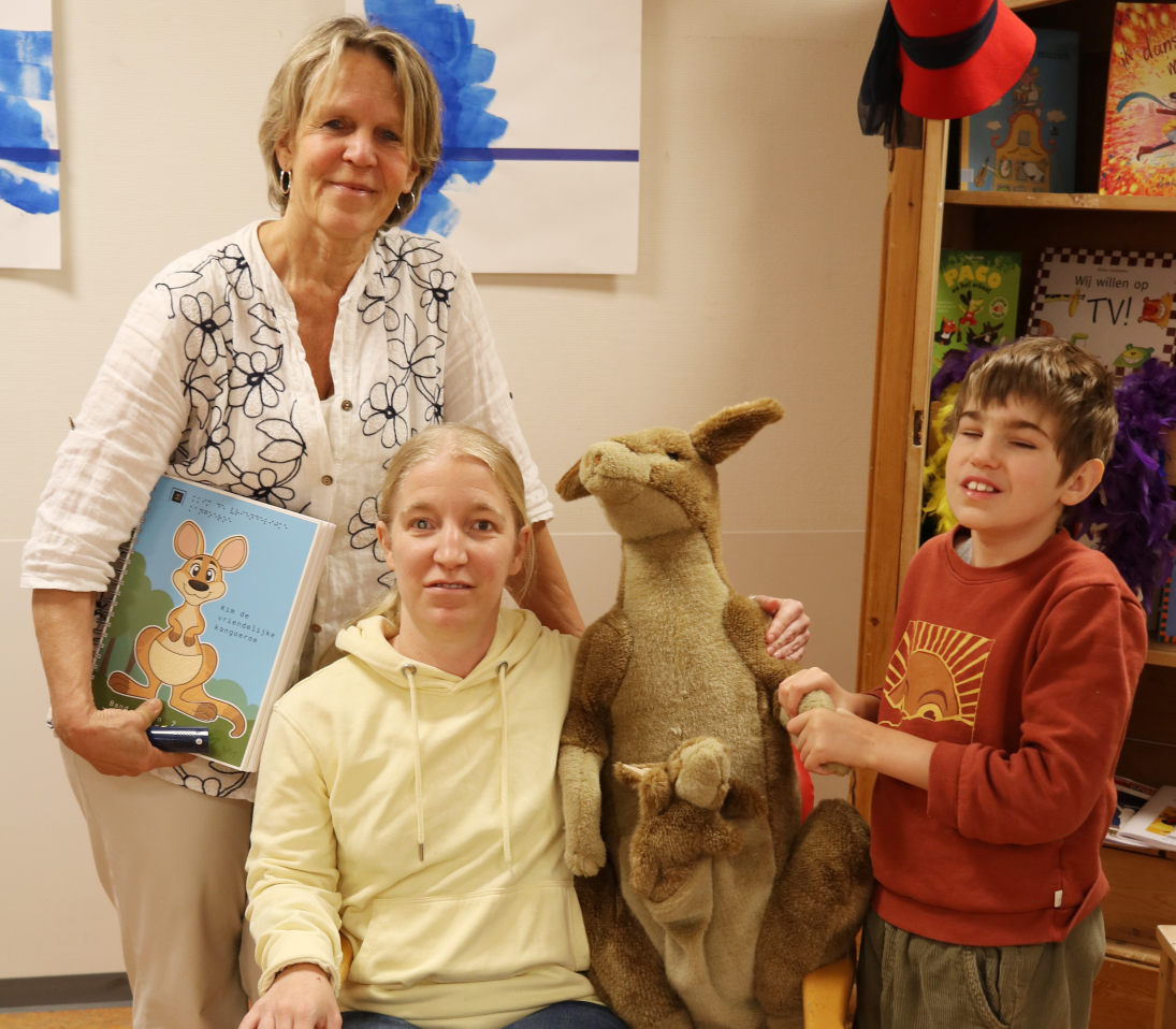 Auteur Hannelies, ervaringsdeskundige Melanie en leerling Jonas op de foto met een knuffel kangoeroe en het boek