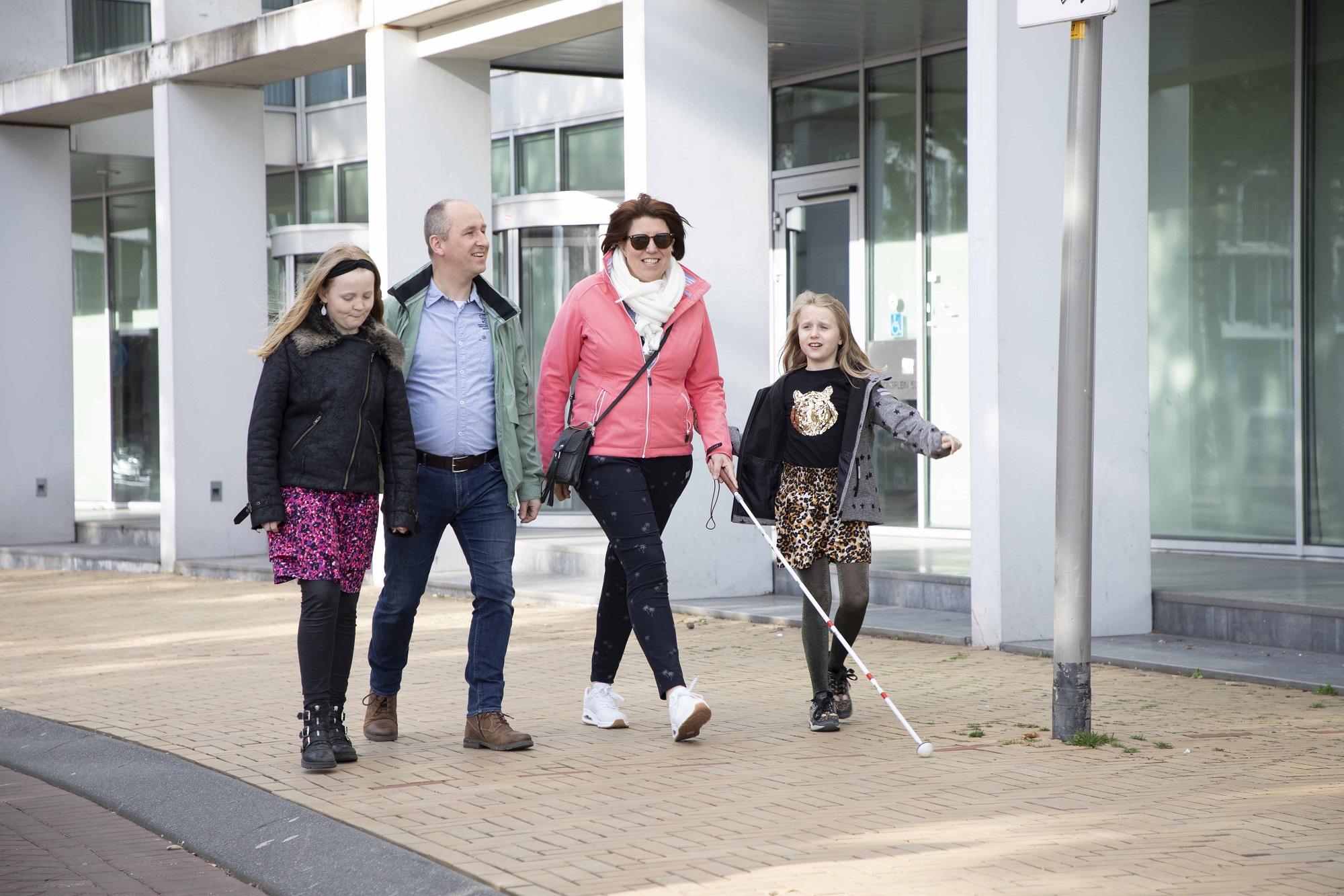 Gezin loopt over straat moeder loopt met een taststok