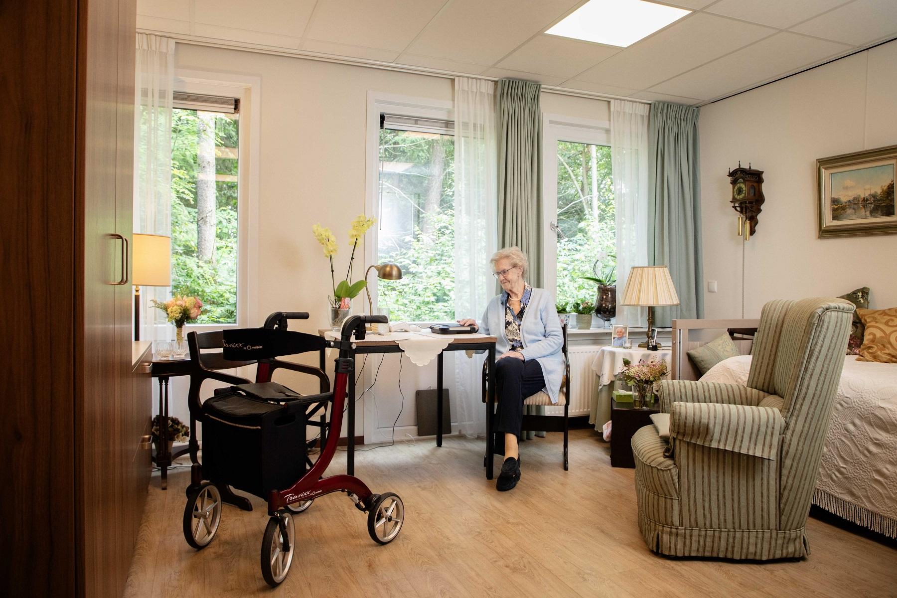 oudere vrouw met rollator zit in woonkamer