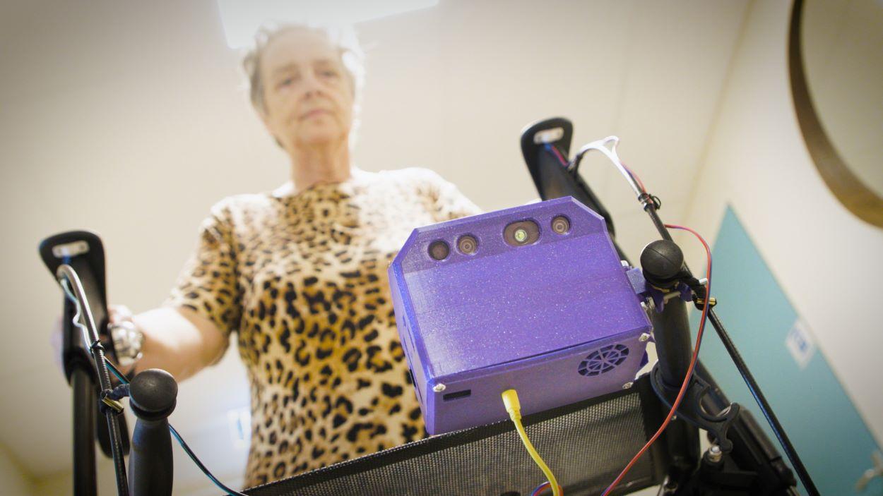 Cliënt met slimme rollator, een paars kastje op de rollator
