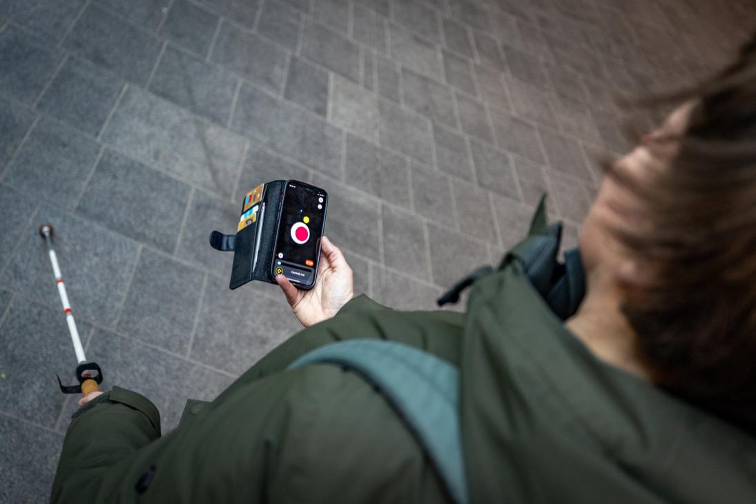 Iemand heeft in de ene hand een taststok en in de andere hand een telefoon met eZwayZ