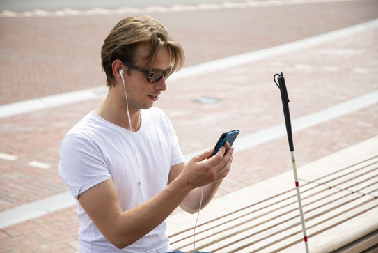 Man taststok en telefoon op een bankje