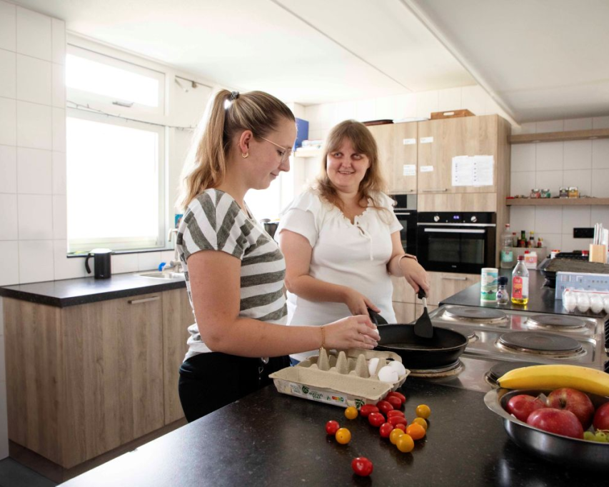Melanie met koekenpan in keuken met begeleider.
