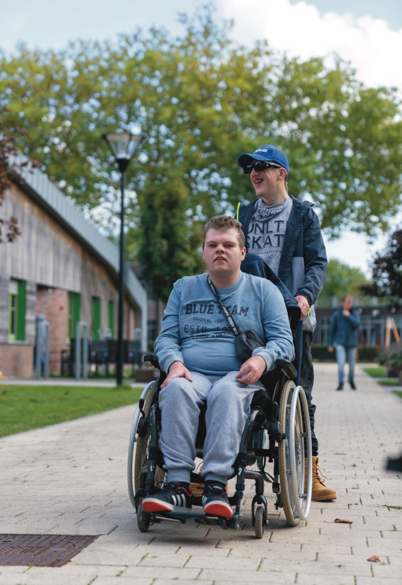 Een bewoner in een rolstoel en een begeleider maken buiten een ommetje