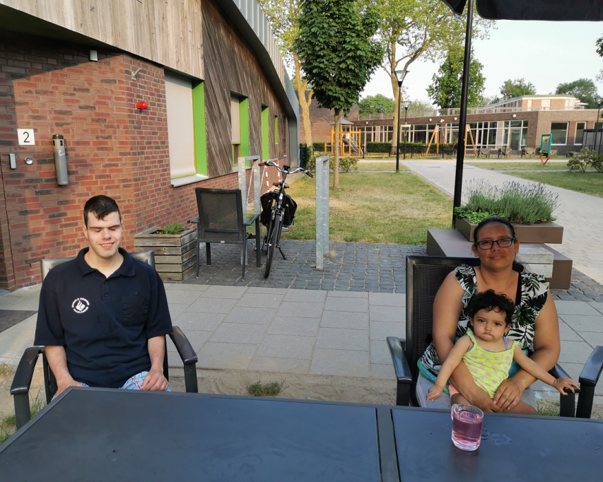 Jeremy en Gina zitten samen buiten aan tafel. Gina heeft haar jongste dochter op schoot.