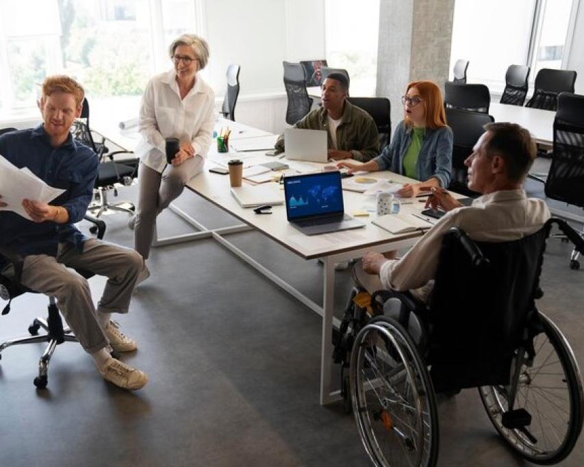 Inclusieve kantoor plek met 5 medewerkers aan een vergadertafel (bron: freepik)